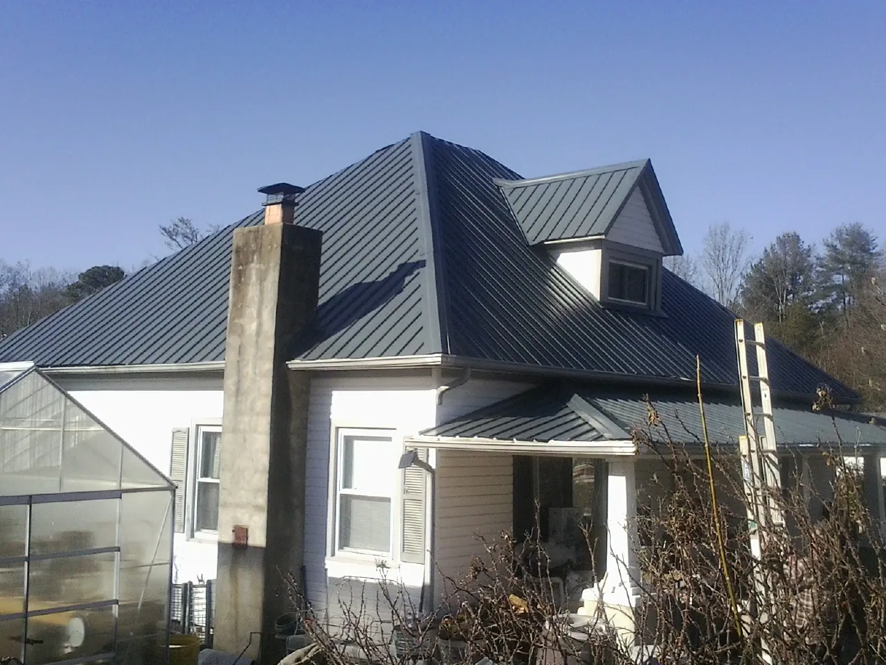 Dark blue standing seam metal roof on a white farmhouse with dormer — Slate & Tile Roof Repair by Roofing Brothers in Mc Gill