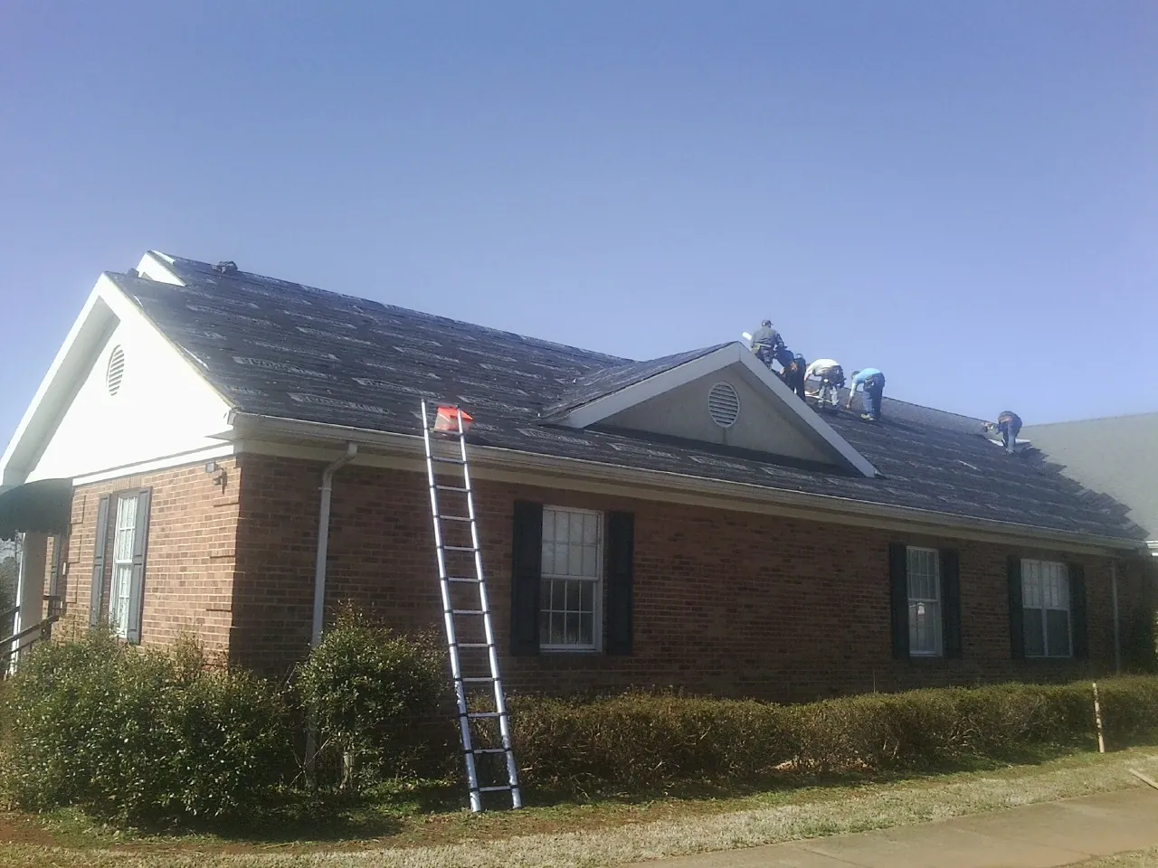 Crew tearing shingles off a brick ranch roof with a ladder set — Emergency Roof Repair work by our crew in Mc Gill