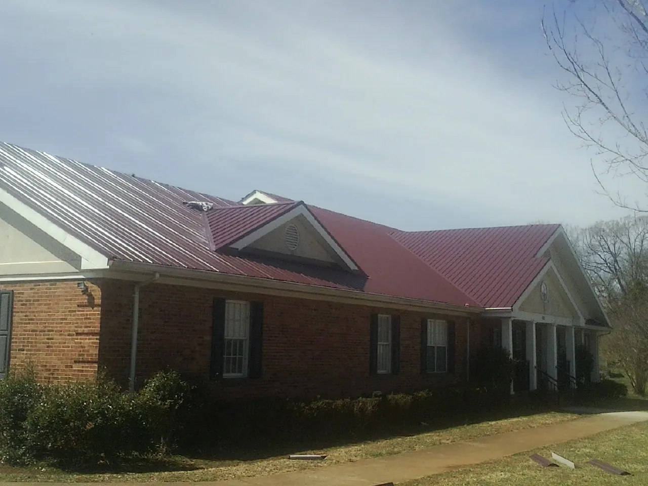 Red metal roof with gabled entries on a long brick building, from a Hail Damage Roof Repair job in Mc Gill