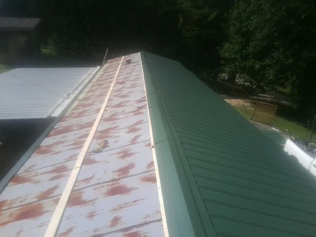 Old rusted panels beside newly installed green metal roofing — Wind Damage Roof Repair by Roofing Brothers in Mc Gill