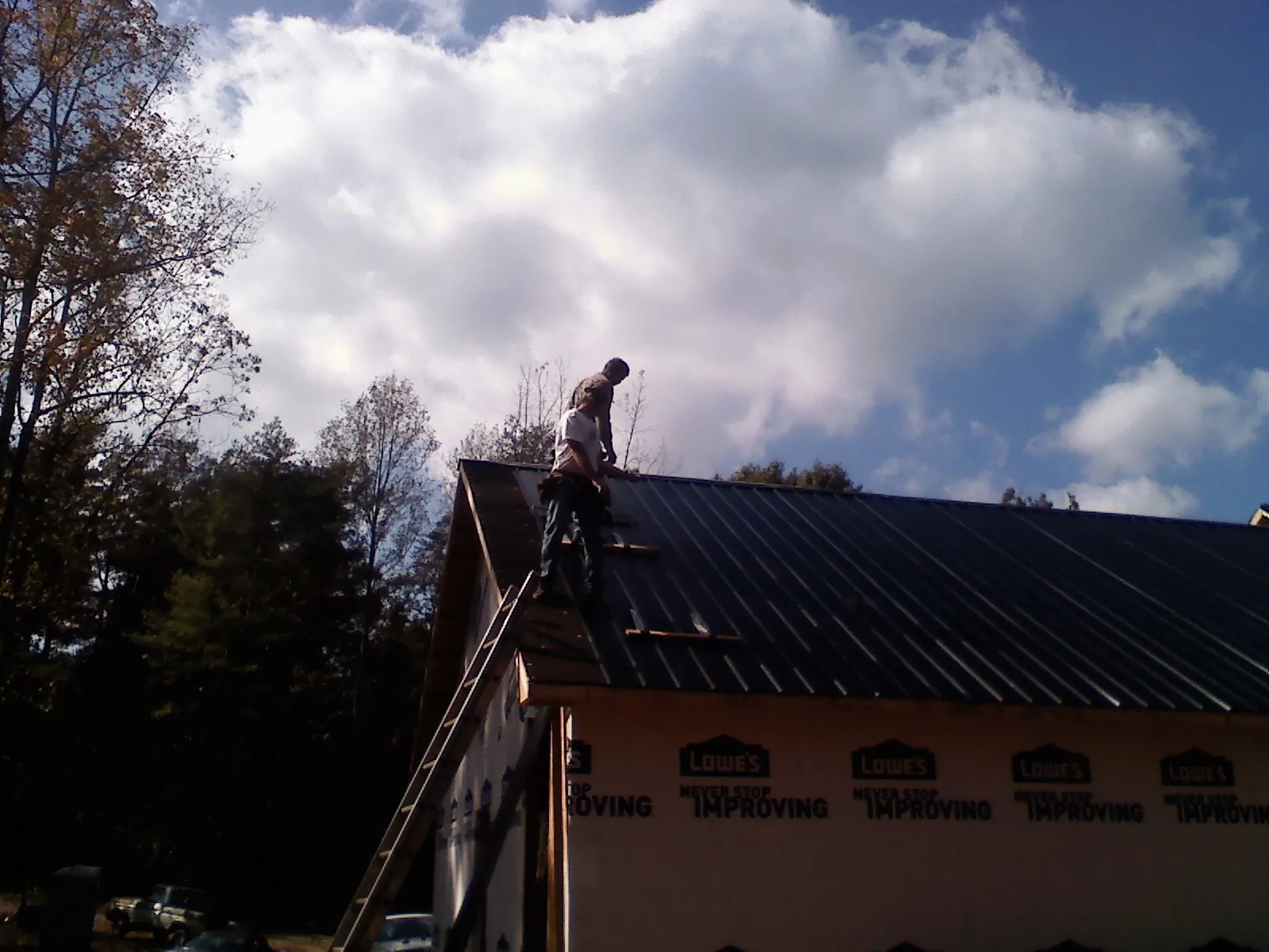 Roofer fastening dark metal panels high against a cloudy sky, from a Roof Inspection job in Mc Gill