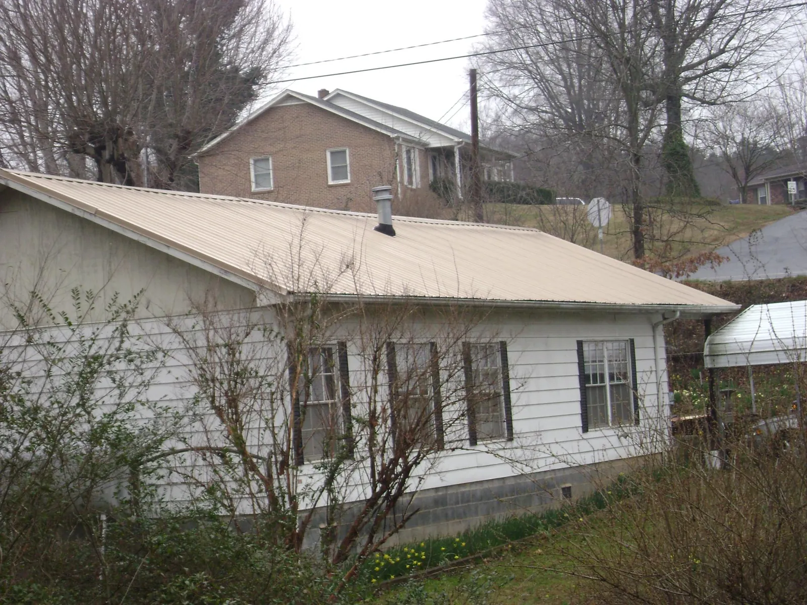 Tan metal roof on a white sided house set into a hillside — Commercial Roofing by Roofing Brothers in Mc Gill