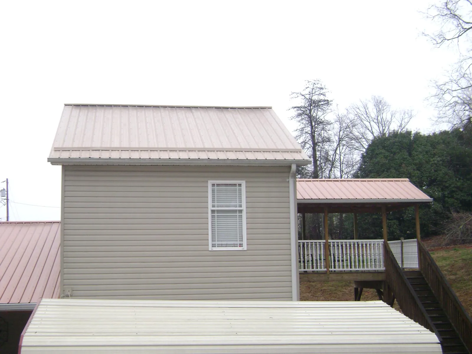 Tan metal roofs on a two story addition and attached porch, from a Roof Replacement job in Mc Gill